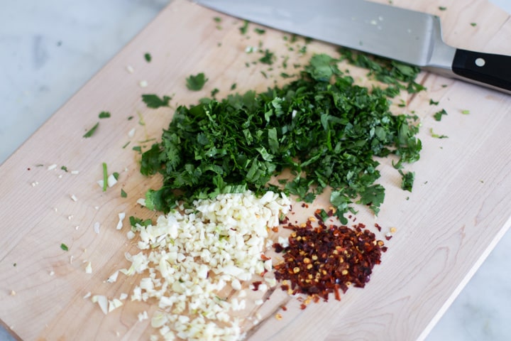 chopped cilantro, garlic, and crushed red pepper on a cutting board