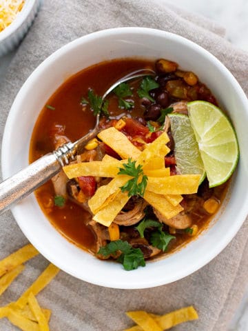 Easy Chicken Tortilla Soup is a hearty, delicious soup filled with chicken, green chile, corn, and black beans in a tomato broth. This soup is full of flavor without being too spicy. Serve it with fried tortilla strips and cheese for the ultimate Tex-Mex lunch or dinner!