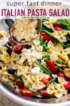 Italian dressing pasta salad in a large bowl with feta cheese being added. pinable image.