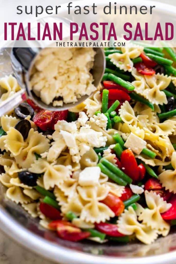 Italian dressing pasta salad in a large bowl with feta cheese being added. pinable image.