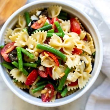 a bowl filled with italian dressing pasta salad with a white towel and wooden spoon in the background