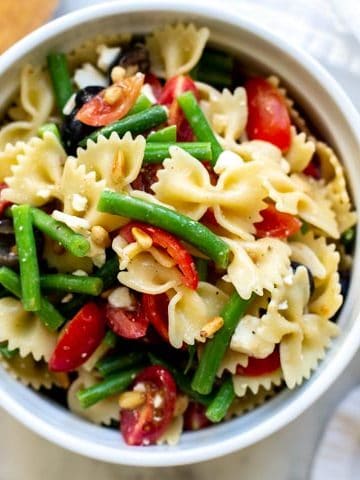 a bowl filled with italian dressing pasta salad with a white towel and wooden spoon in the background