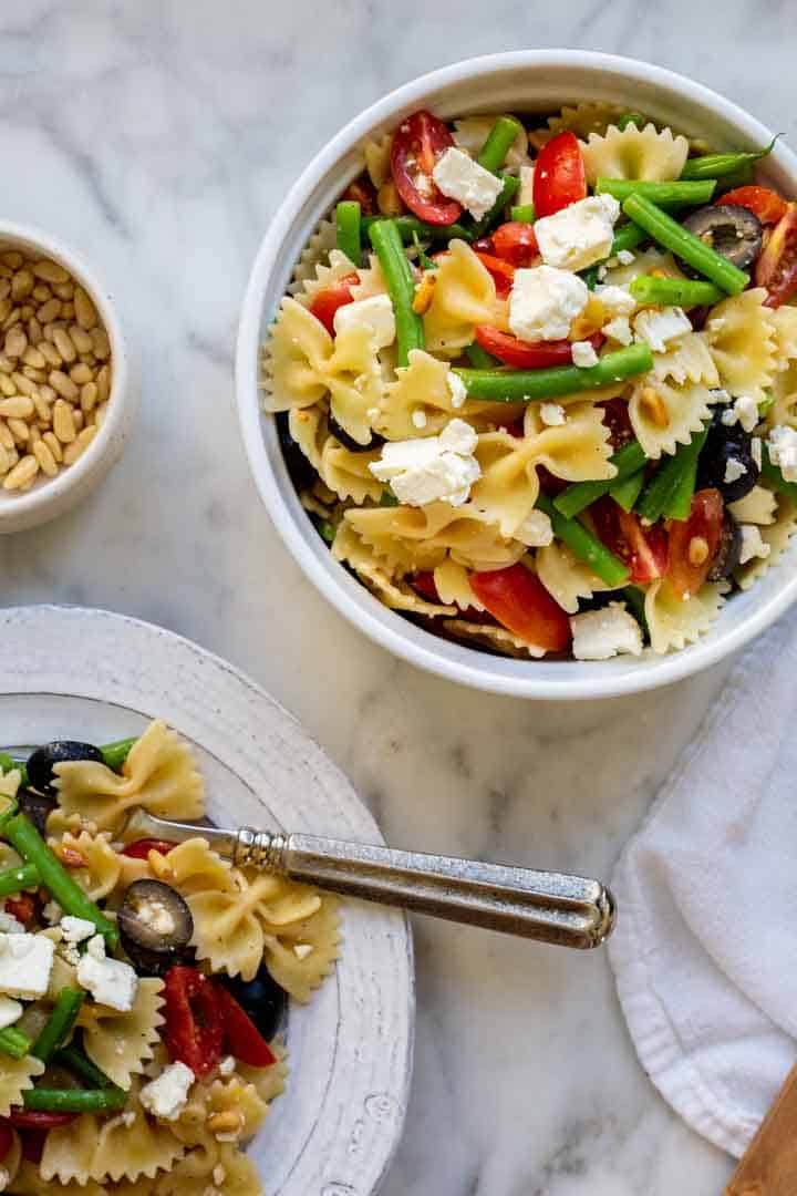 a bowl and plate filled with Italian dressing pasta salad with pine nuts in a small bowl