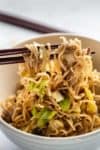 a bowl of ramen noodles dangling from chopsticks