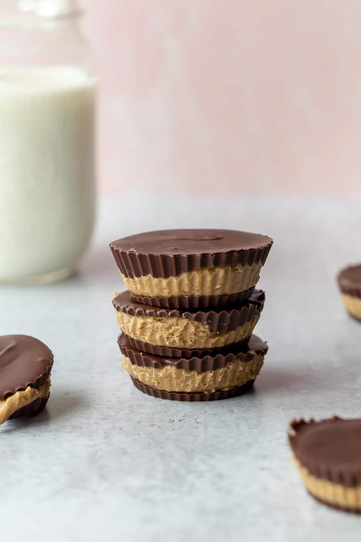 3 sunbutter cups stacked on a gray surface with a glass of milk in the background