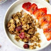 Granola and sliced strawberries over yogurt in a white bowl