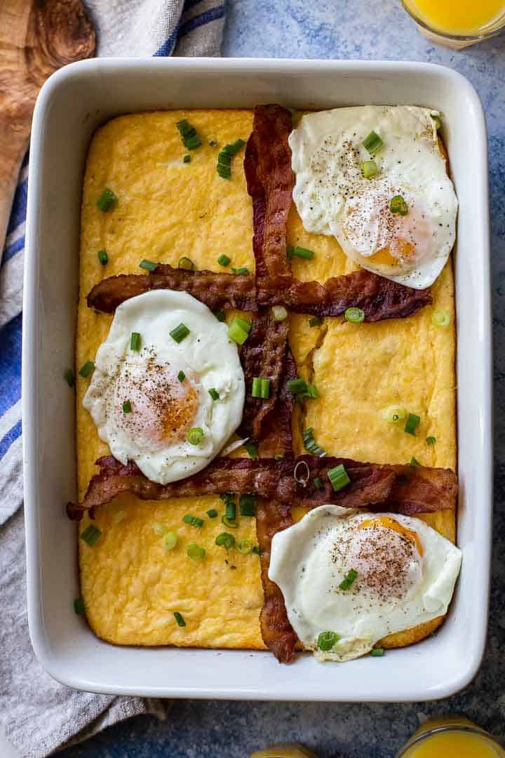 white casserole pan with grits, bacon strips and 3 fried eggs