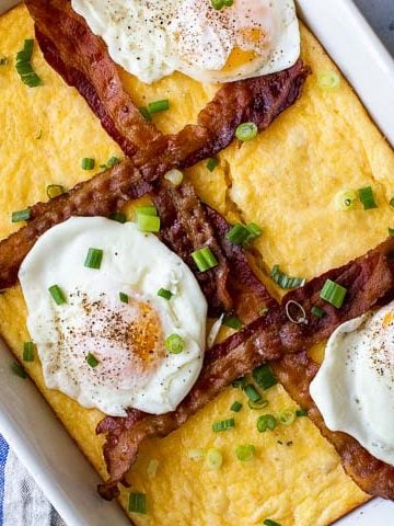 grits recipe in white casserole dish topped with bacon strips and fried eggs
