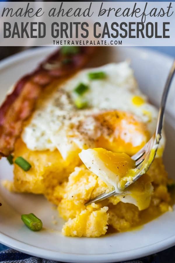 a fork taking a bite of an egg over grits casserole with a piece of bacon in the background