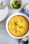 corn casserole in a round white baking dish-sliced green onions in background