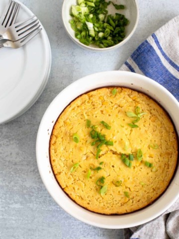 corn casserole in a round white baking dish-sliced green onions in background