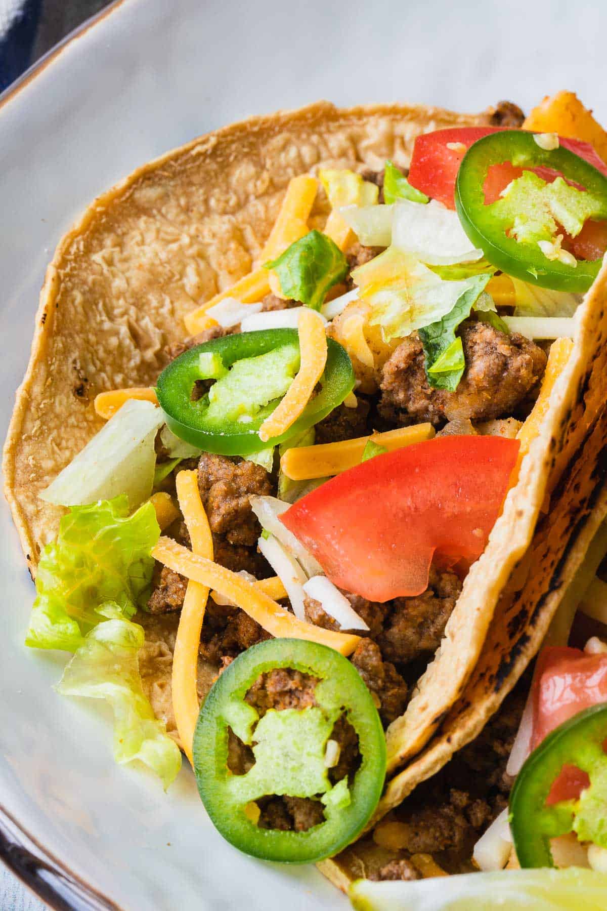 close up of a taco in a corn tortilla and topped with lettuce, tomato, cheese and jalepeno