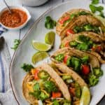 several tacos on a white platter with a bowl of salsa in the background