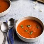 a bowl of tomato basil soup with two spoons on the left