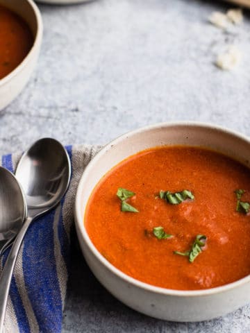 a bowl of tomato basil soup with two spoons on the left