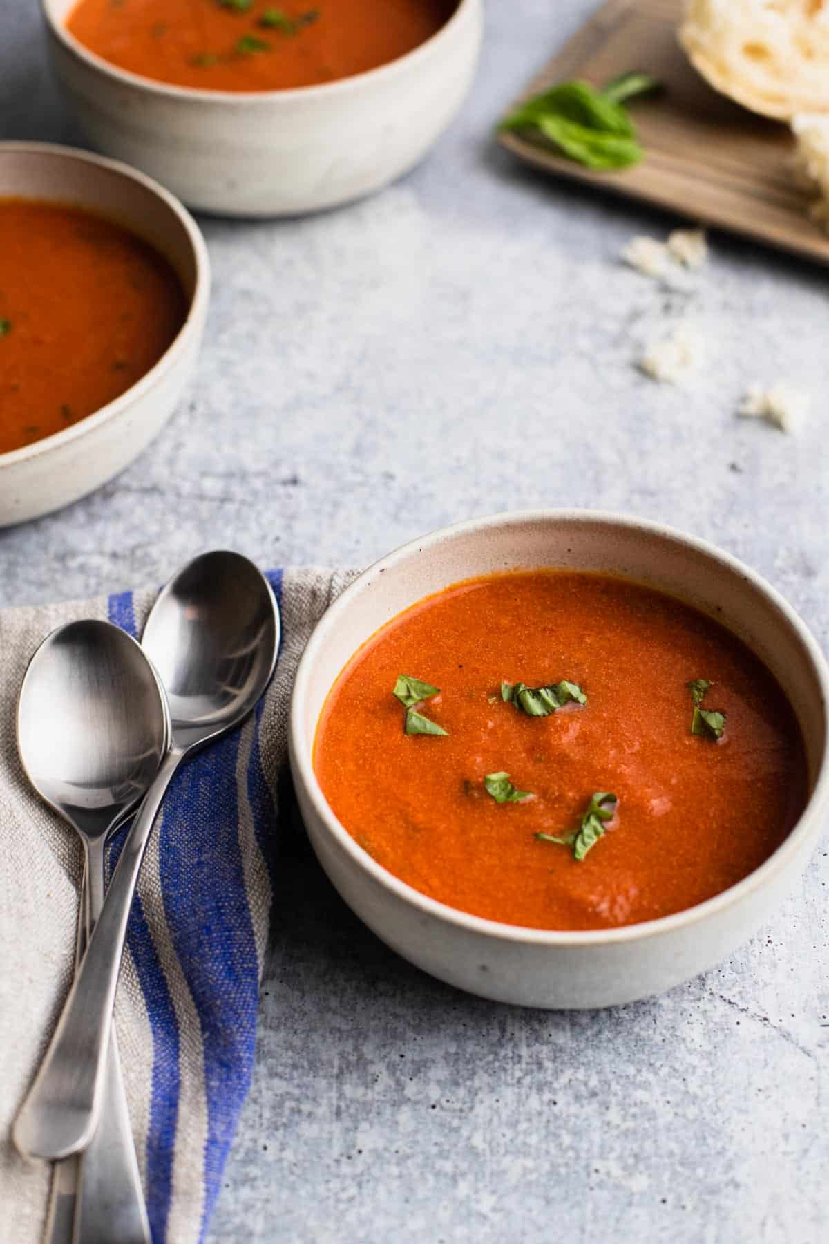 a bowl of soup with two spoons on left and extra bowls and bread in the background