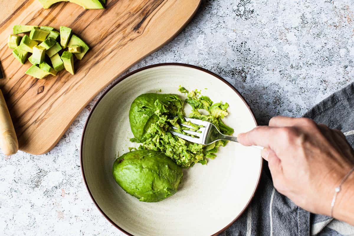 overhead shot of avocado in a bowl being mashed with a fork