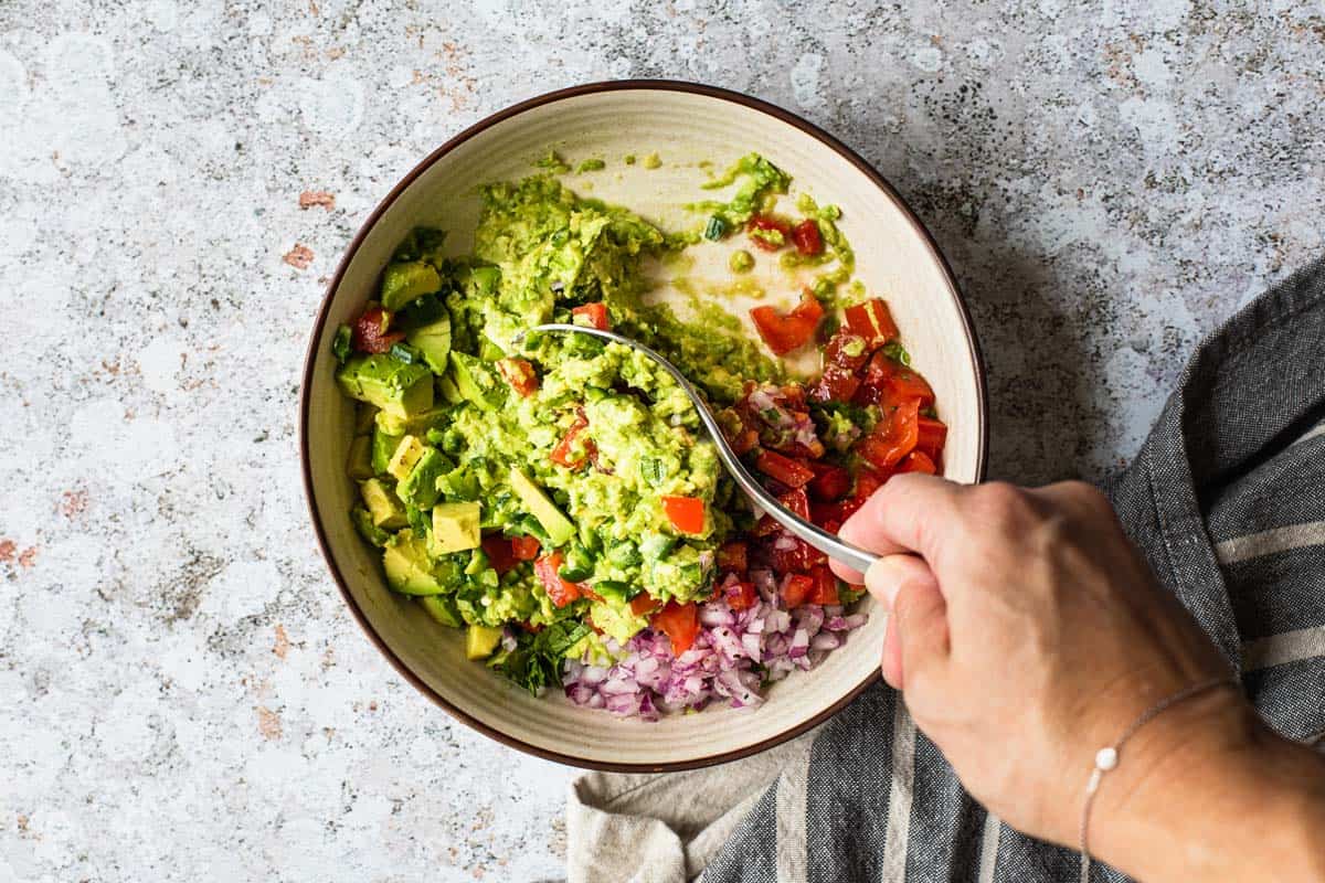 mixing ingredients in a bowl of mashed avocado