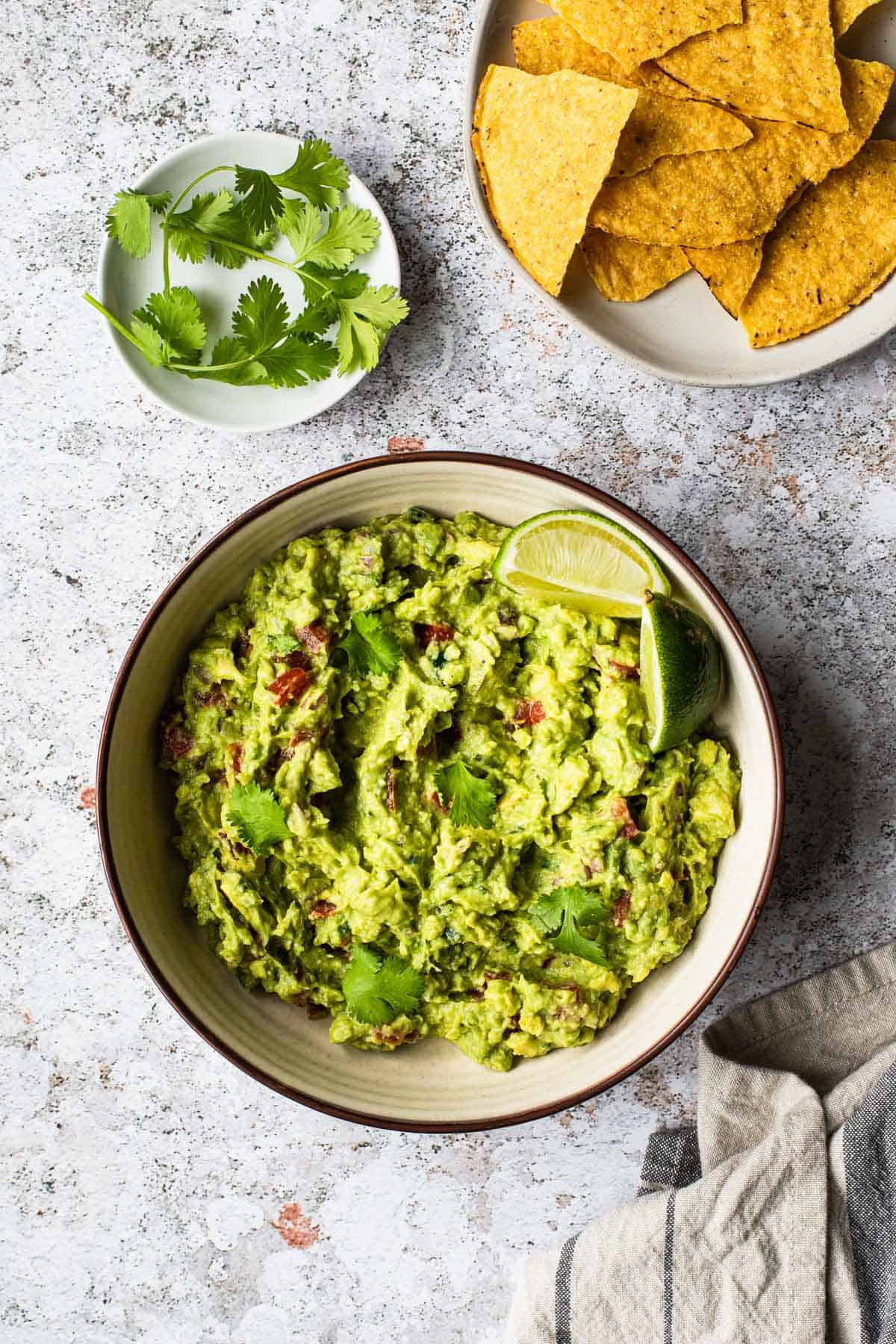 overhead view of a bowl of guacamole with cilantro leaves and chips in the background