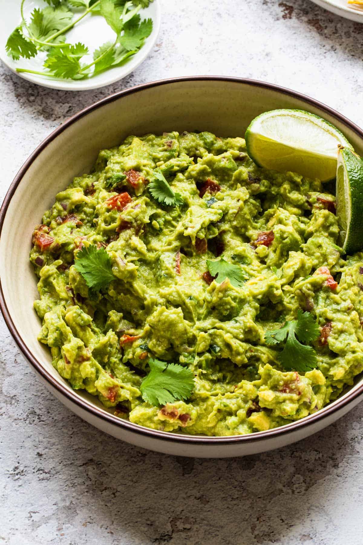  close up view of bowl of guacamole with cilantro leaves in background