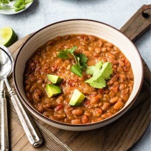 bowl of pinto beans on a wooden board with spoons to the left