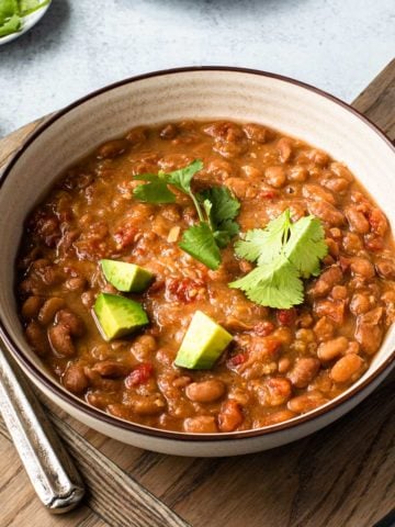 bowl of pinto beans on a wooden board with spoons to the left