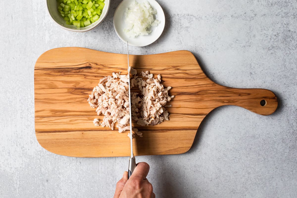 overhead view of cutting board with chicken being chopped-celery and onion in background