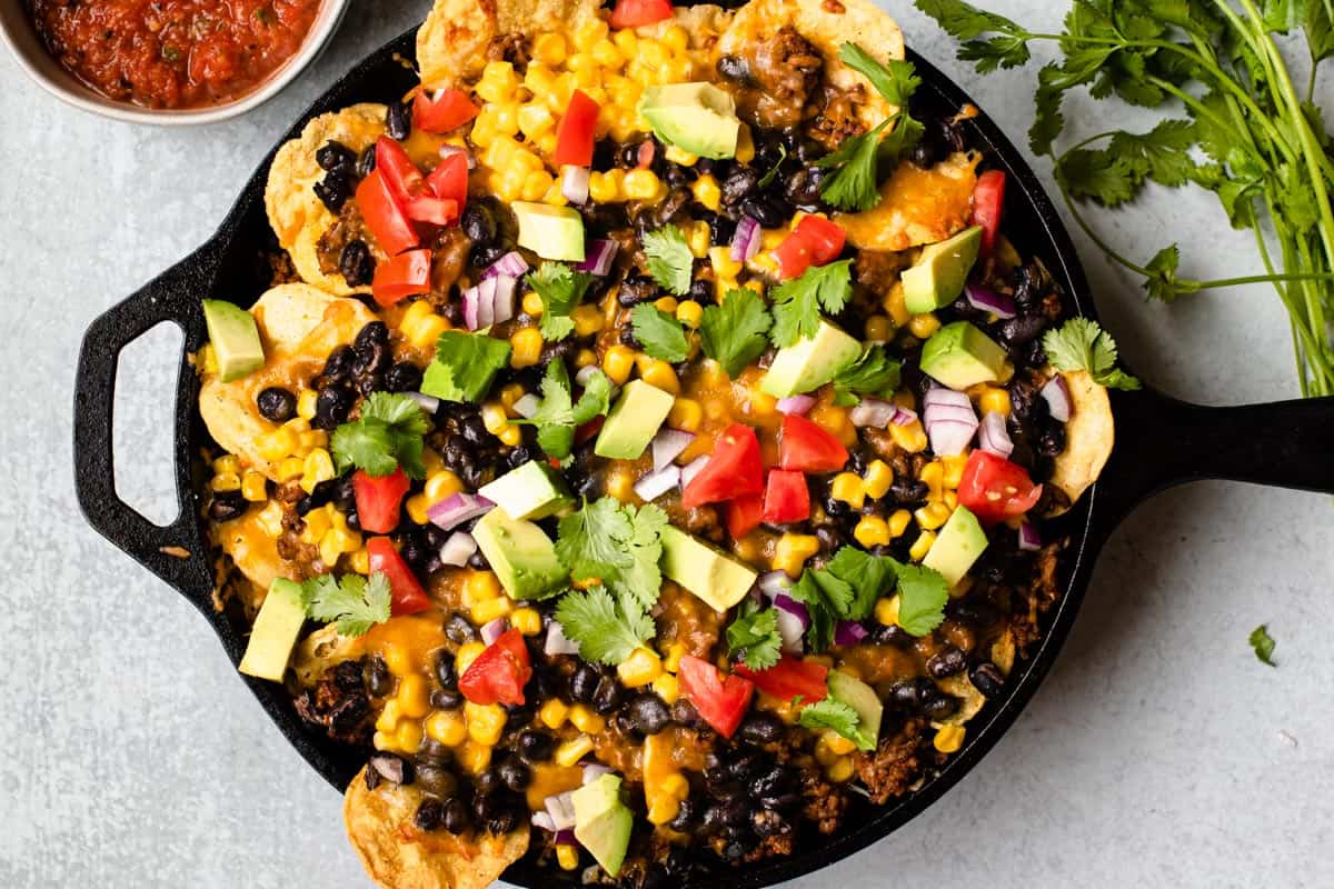 skillet filled with nachos and garnished with tomato, avocado, onion, cilantro