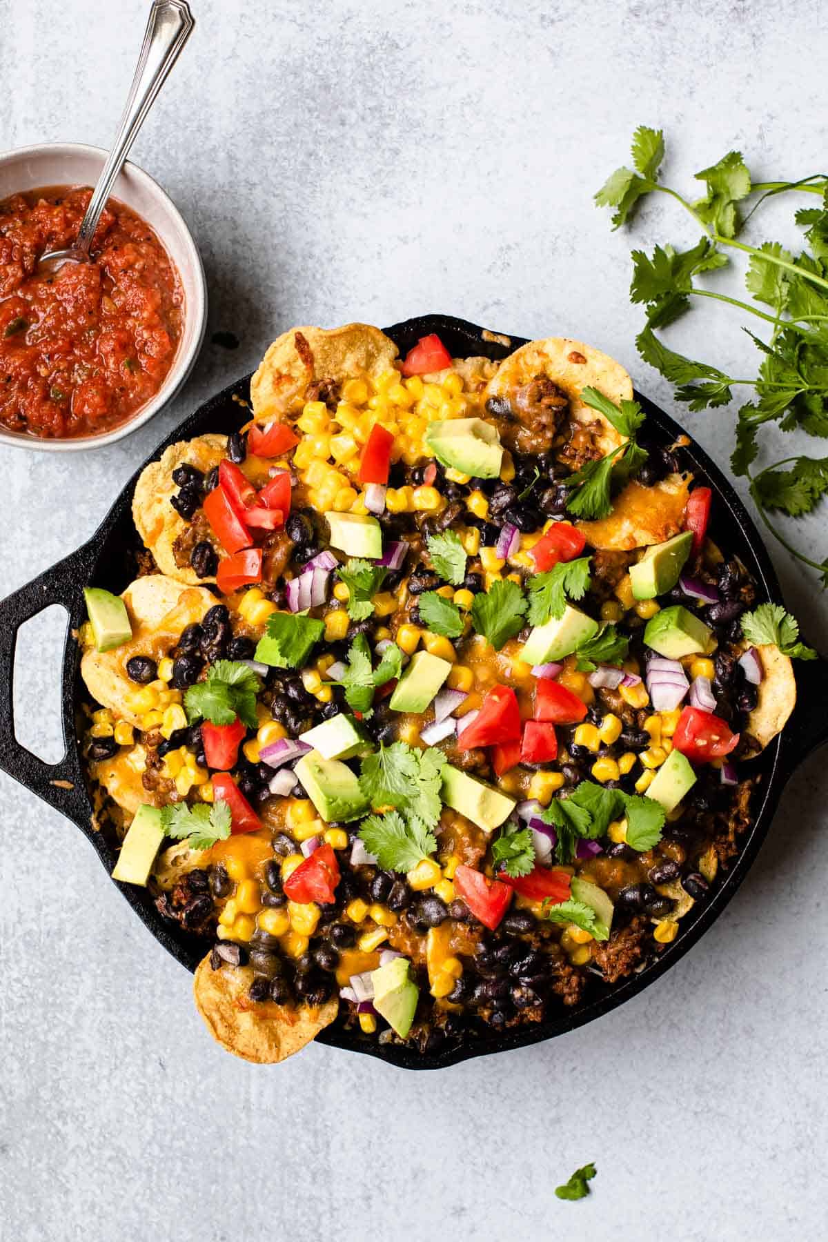 baked nachos in a cast iron skillet with salsa in the background