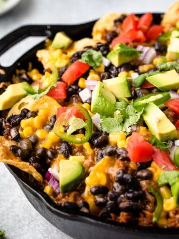 close up view of nachos in a cast iron skillet loaded with garnishes