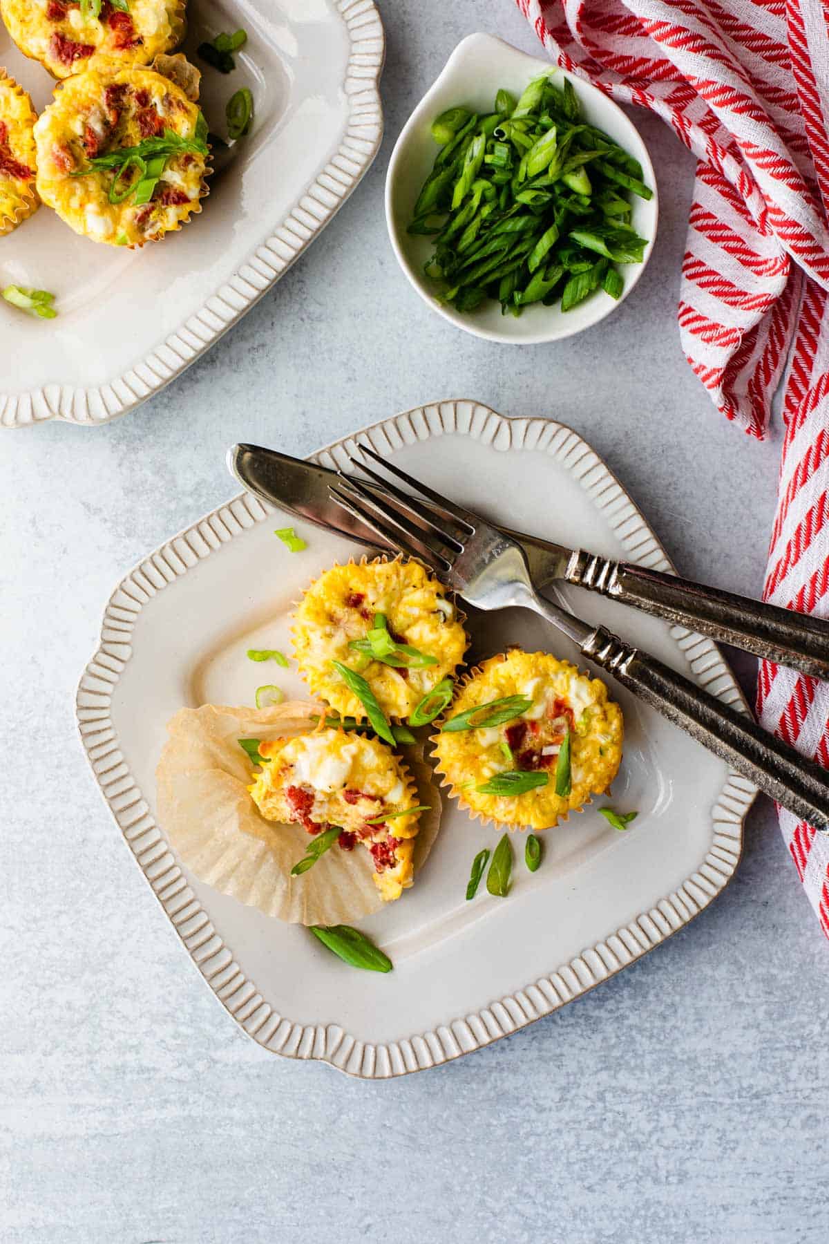 egg cups on two plates with green onions and a red and white stripped dishcloth