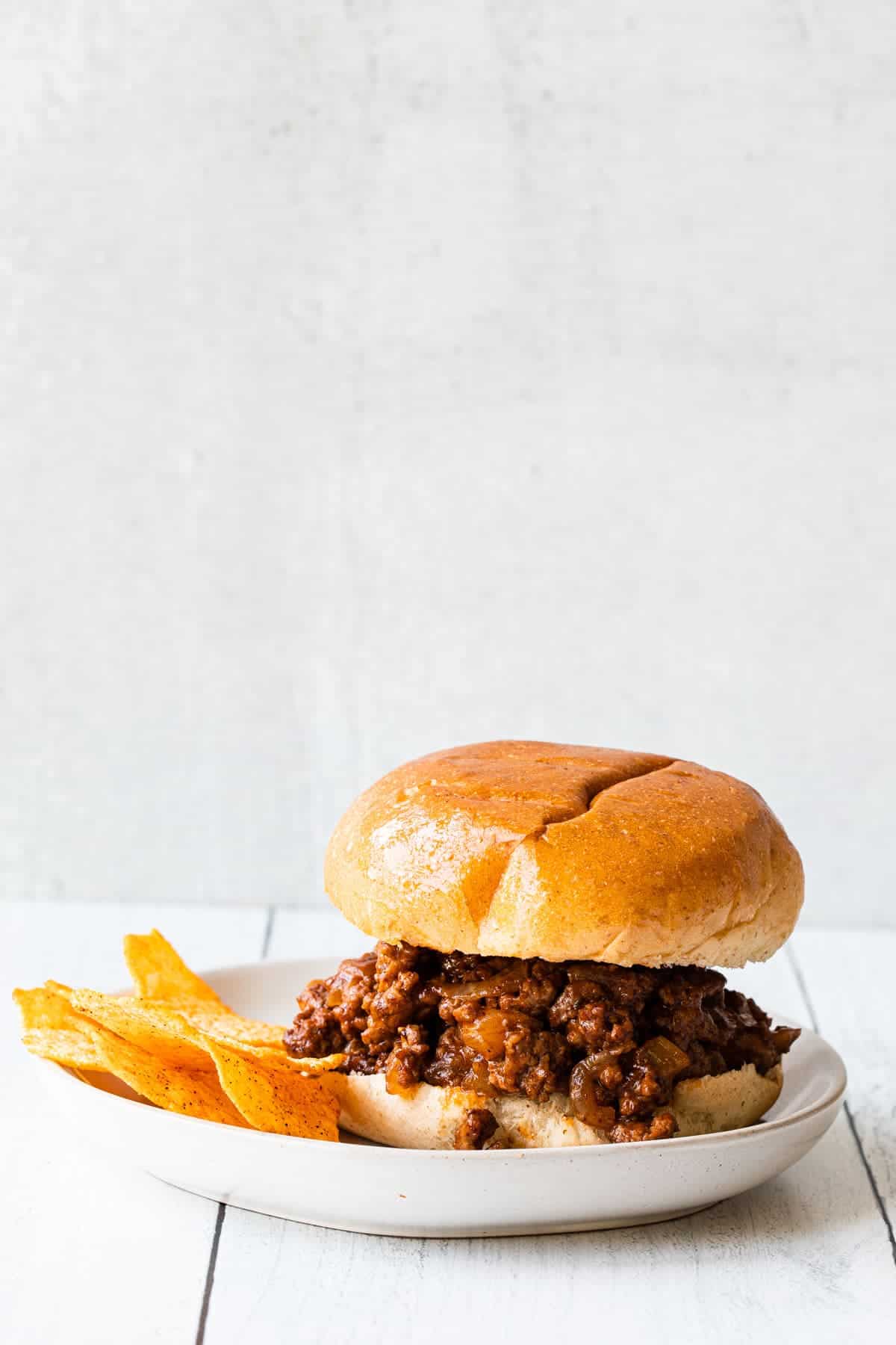 straight on view of sloppy joe sandwich with a side of bbq chips-gray background