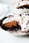a chocolate pie topped with whipped cream with a slice taken out and set in background