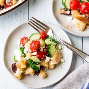 mediterranean bread salad on a white plate with a fork and a small plate in background