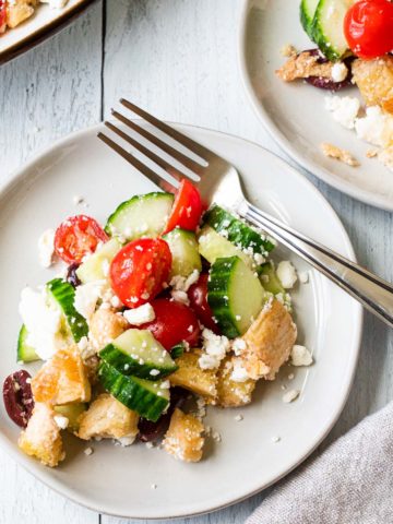 mediterranean bread salad on a white plate with a fork and a small plate in background