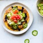 one vegetarian tostada on a white plate with guacamole and sliced jalepenos