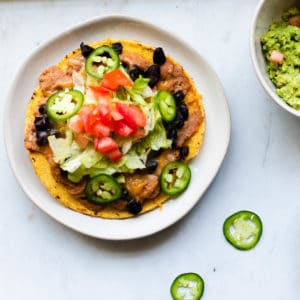 one vegetarian tostada on a white plate with guacamole and sliced jalepenos