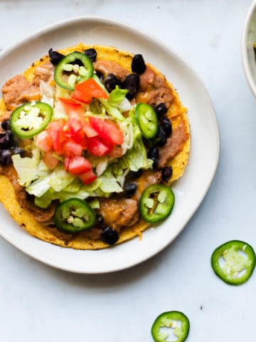 one vegetarian tostada on a white plate with guacamole and sliced jalepenos