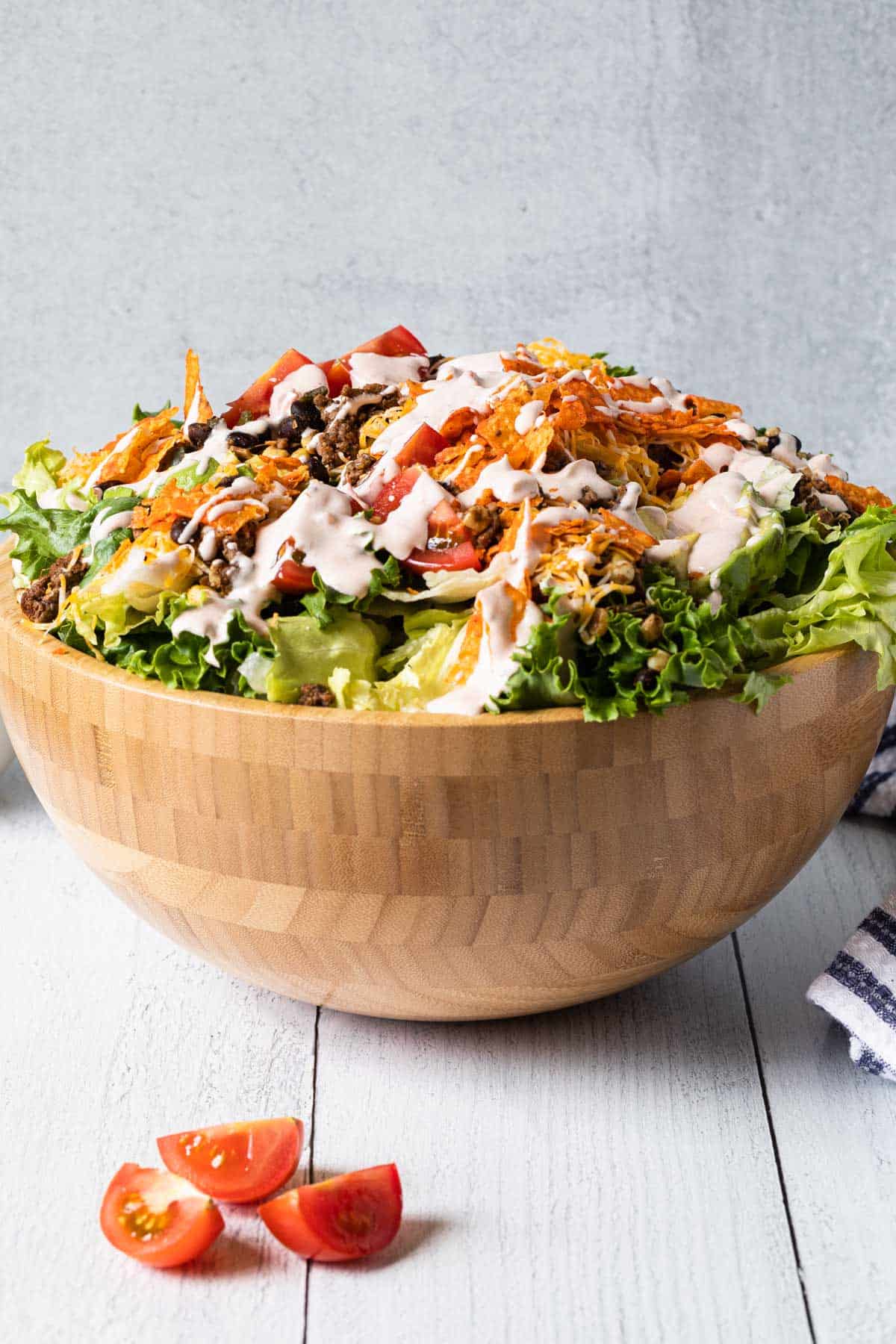 a large wooden bowl overflowing with taco salad drizzled with creamy dressing