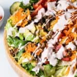 close up overhead view of wooden bowl filled with salad drizzled with creamy dressing