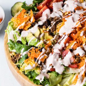 close up overhead view of wooden bowl filled with salad drizzled with creamy dressing