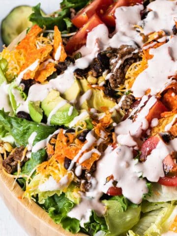 close up overhead view of wooden bowl filled with salad drizzled with creamy dressing