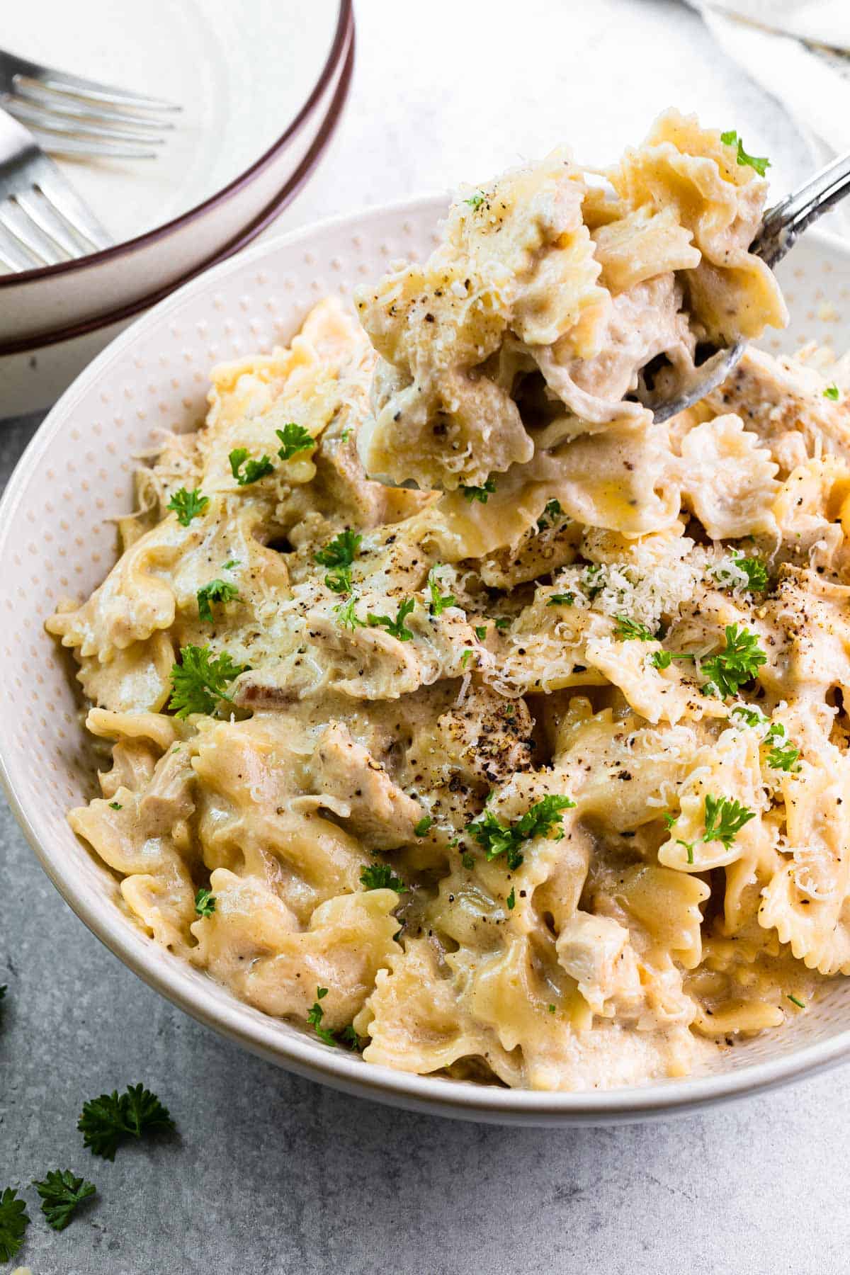 close up view of a fork taking a bite out of a white bowl filled with pasta in a creamy white sauce