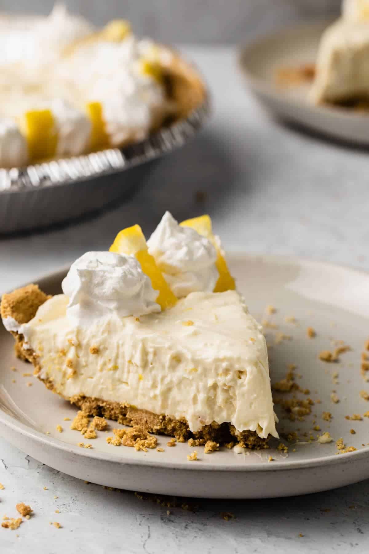 close up view of a slice of lemon pie on a white plate with whole pie in background