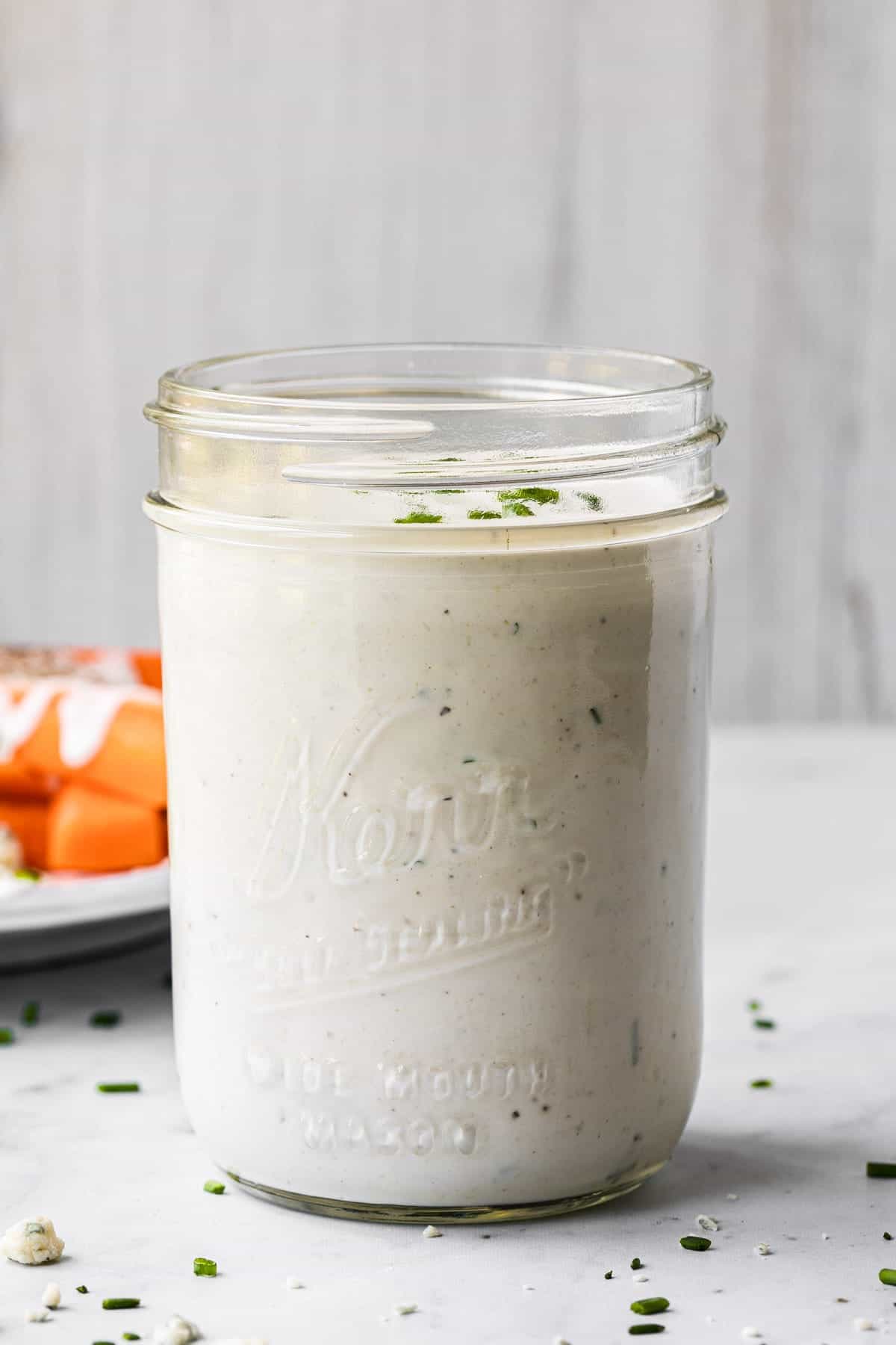 straight on view of dressing in a glass mason jar with a plate of carrots in background