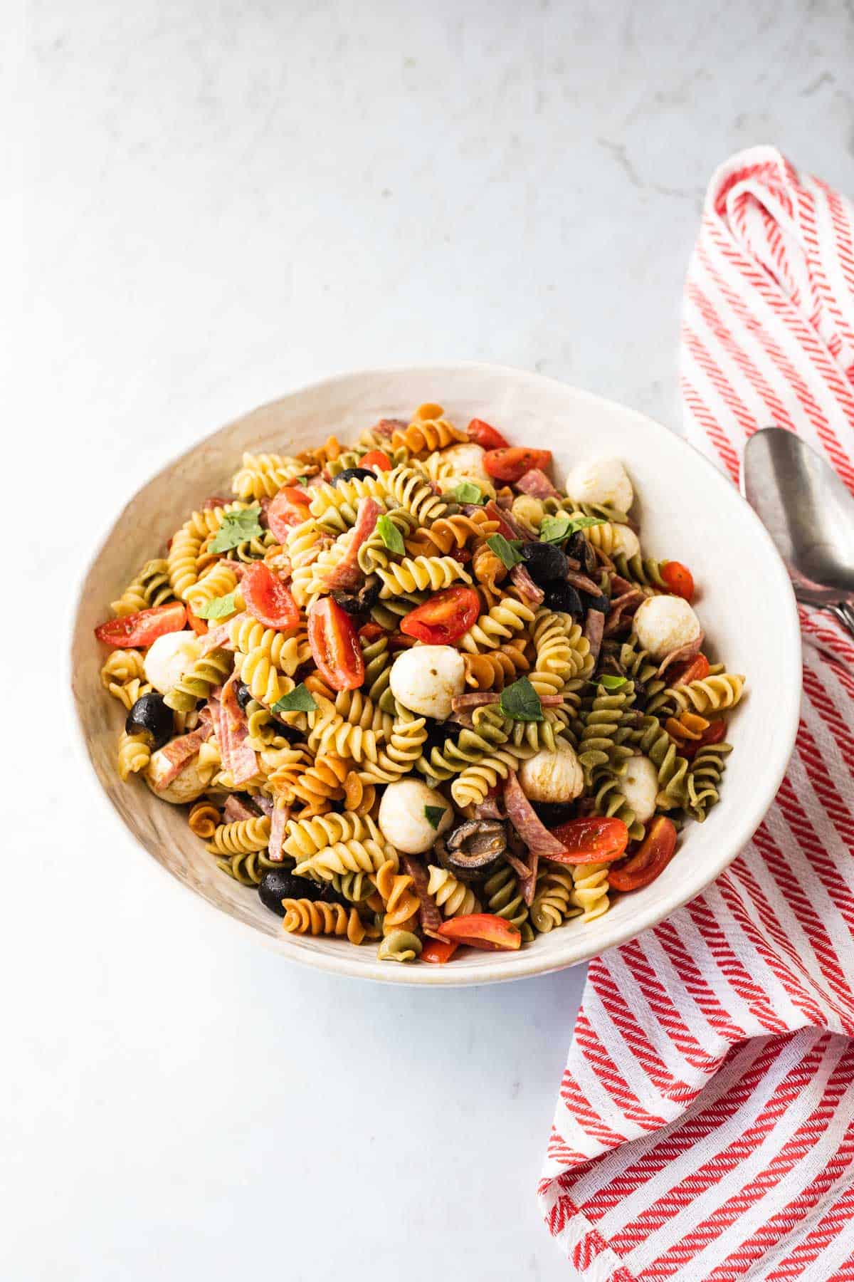 white bowl with a pasta salad in it, red and white striped towel on right side