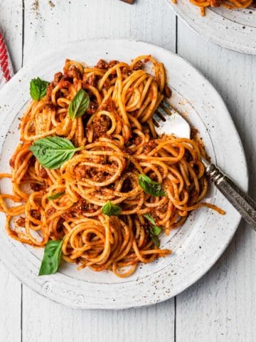 overhead view of a plate of spaghetti with basil leaves