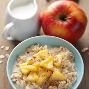 apple oatmeal in a bowl with milk and red apple in background