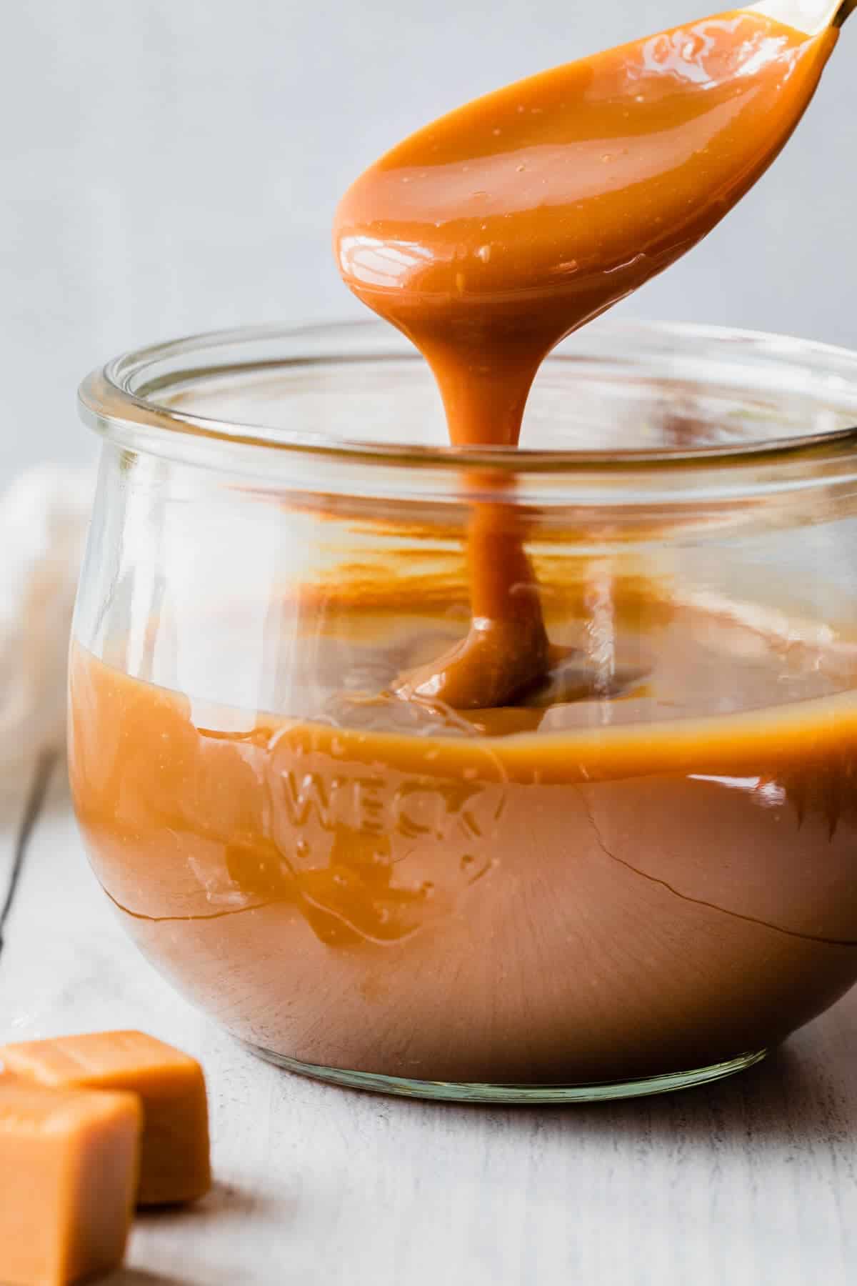 caramel sauce drizzling off a spoon into a glass jar