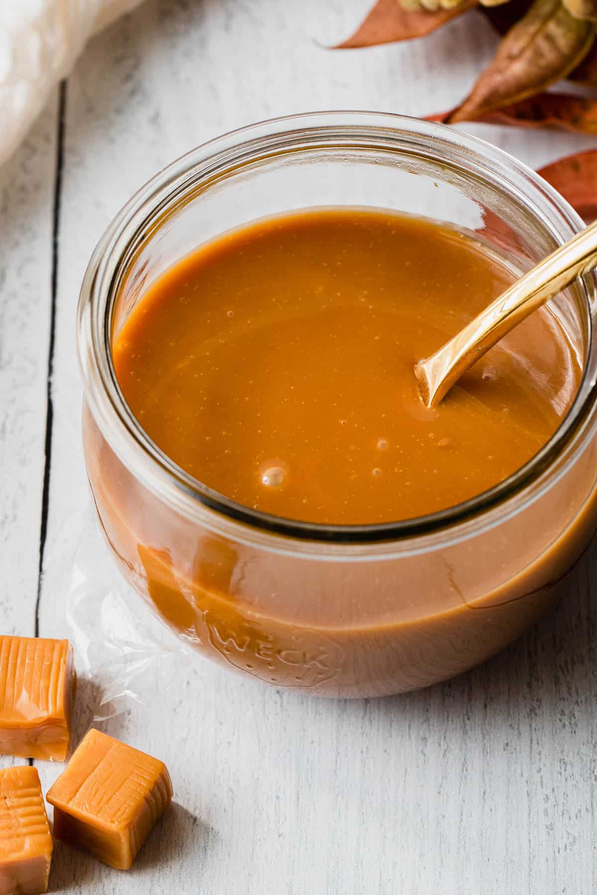 close up overhead shot of caramel sauce in a glass jar with a gold spoon